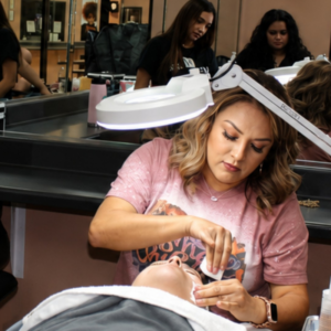 Esthetician student performing a facial treatment under a magnifying lamp at Houston Training Schools.